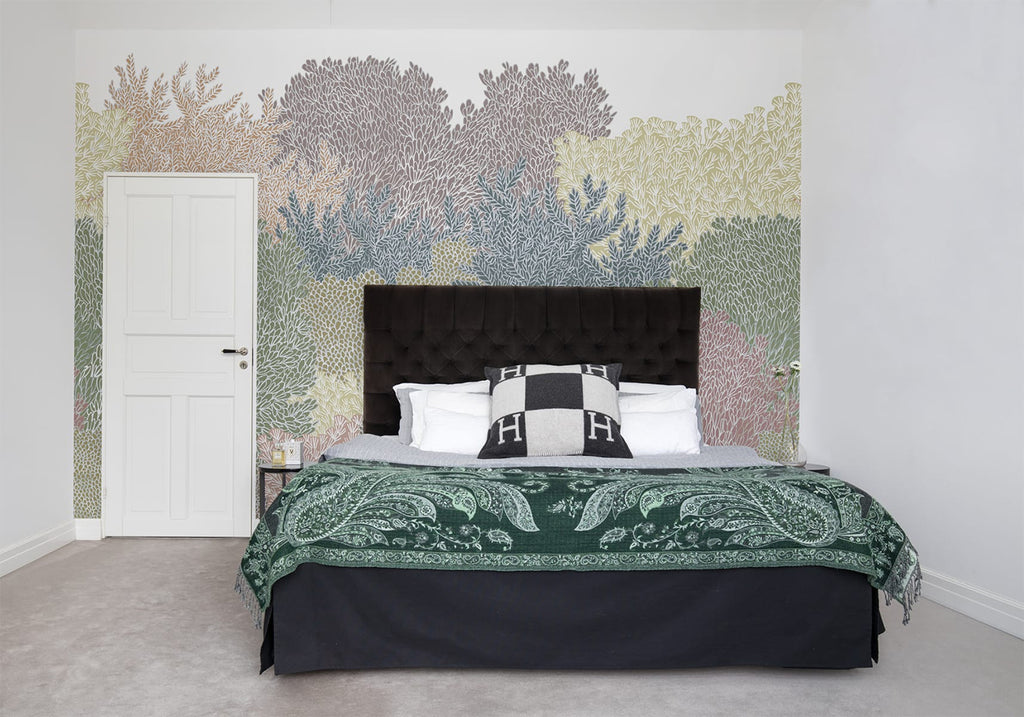 Alice Garden, Mural Wallpaper in multicolor featured on a wall of a bedroom with a bed that has green throw blanket and black headboard