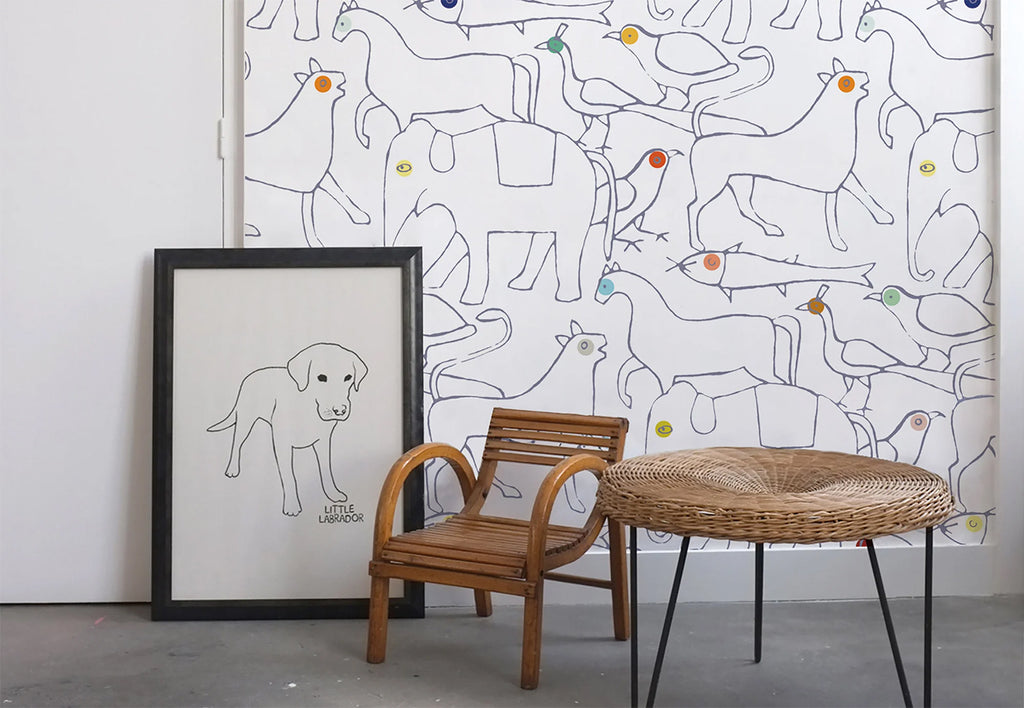 A room featuring Animal Shapes, Pattern Wallpaper with various outlined animals. A framed dog sketch, a wooden chair, and a wicker table add charm to the space.