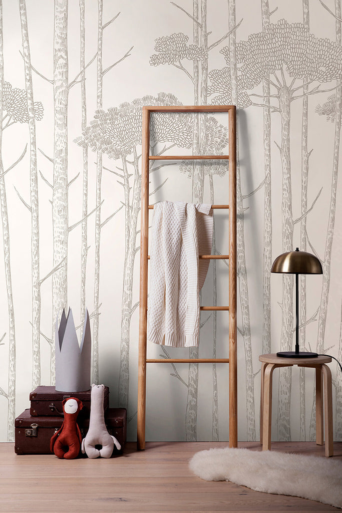 Ara's Birch Trees, Mural Wallpaper in Light Grey featured in a room that is adorned with a wooden ladder, a towel, a lamp atop a wooden stool, and two stacked brown briefcases beside the ladder.