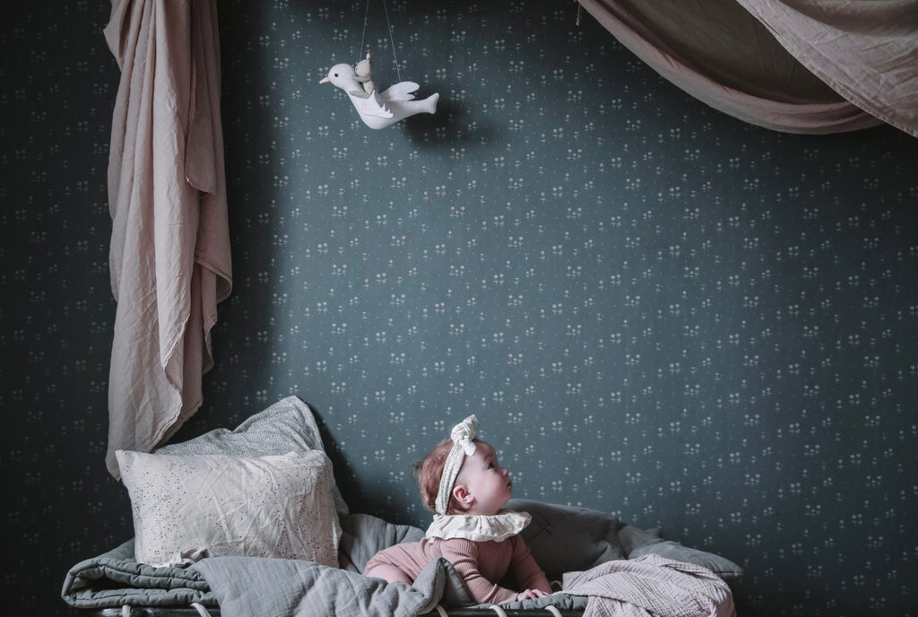 Bianca, Floral Pattern Wallpaper in Stratos Grey Featured on a wall of a kd’s room with several soft pillows and sheets