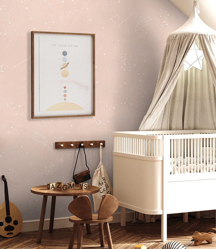A tranquil nursery room bathed in soft pastel hues. The room features a white crib with delicate star details, and a small table. A framed print of the solar system adorns the wall above, adding an educational touch to the room. Chalky Stars, Pastel Pattern Wallpaper in Blush Pink subtly enhances the serene ambiance, creating a perfect environment for both learning and rest.