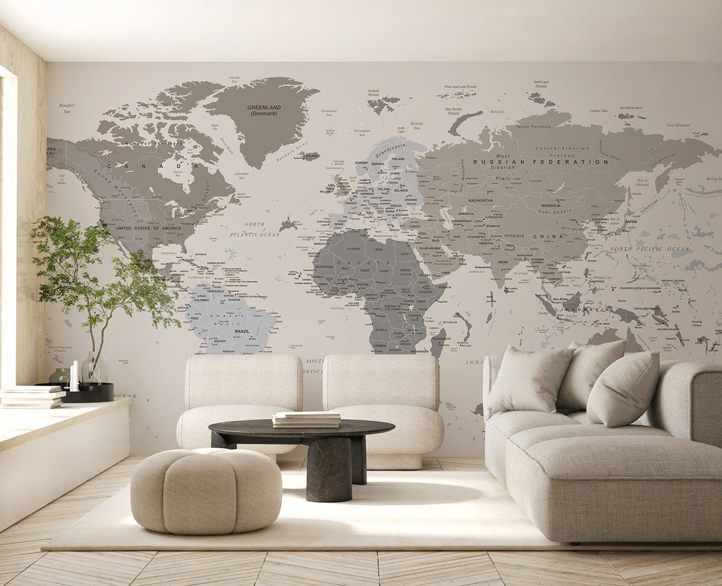 A modern, minimalist room bathed in soft natural light. A large, comfortable light grey sectional sofa takes center stage, paired with a round black coffee table. A small green plant adds a touch of nature, resting on a white sideboard. The room’s sophistication is subtly enhanced by the Classic Atlas World Map Mural Wallpaper.