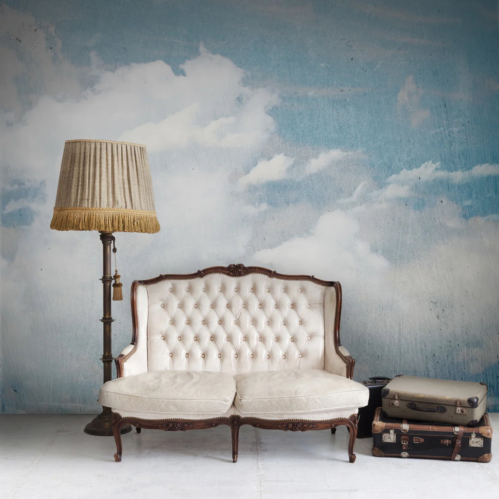 Clouds Above, Mural Wallpaper featured on a wall of a vintage white sofa with wooden base, beside it are stacked briefcase in its left and a lamp stand at the right