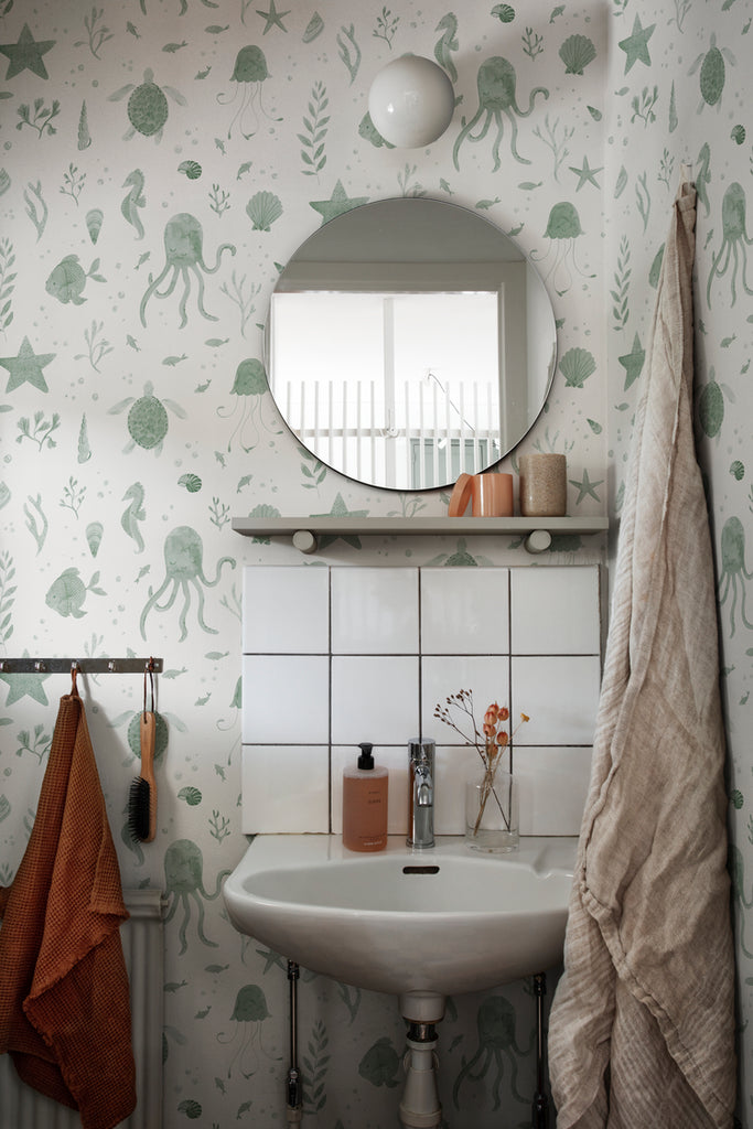 Corals and Friends, Wallpaper in Dark Green Featured on a wall of a toilet, with a round mirror and a lavatory with several products on top of it