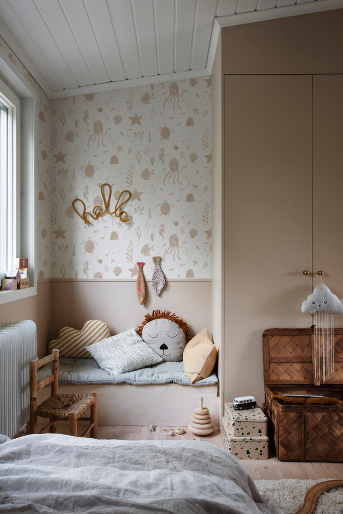 Corals and Friends, Wallpaper in Nude Featured on a wall of a kid’s room with soft pillows and items for kids