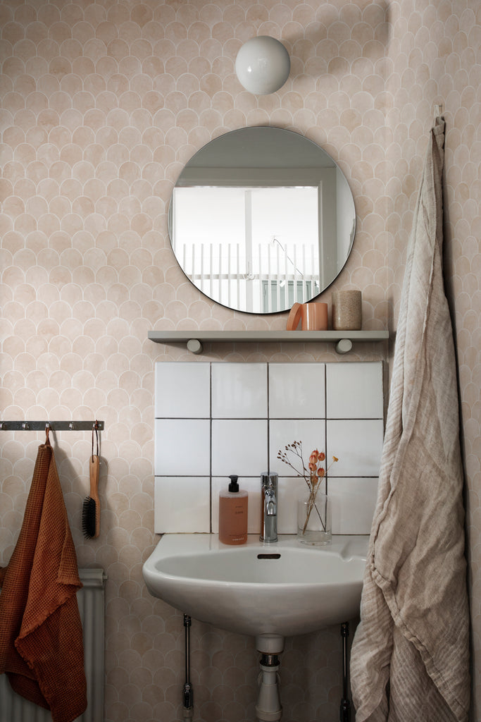 Igor Shells, Pattern Wallpaper in nude featured on a wall of a bathroom with  a round mirror and a circular wall lamp
