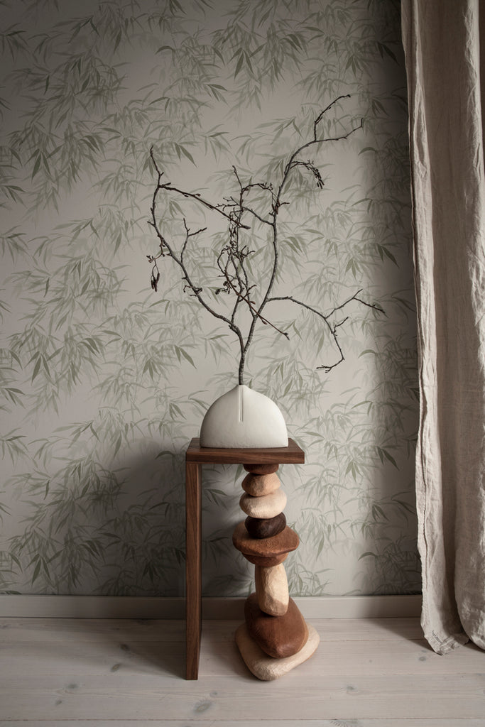 Jon Watercolor Bamboo Japanese Wallpaper in Green Featured on a wall of a room with stacked stone art that holds a ceramic vase on a wooden base