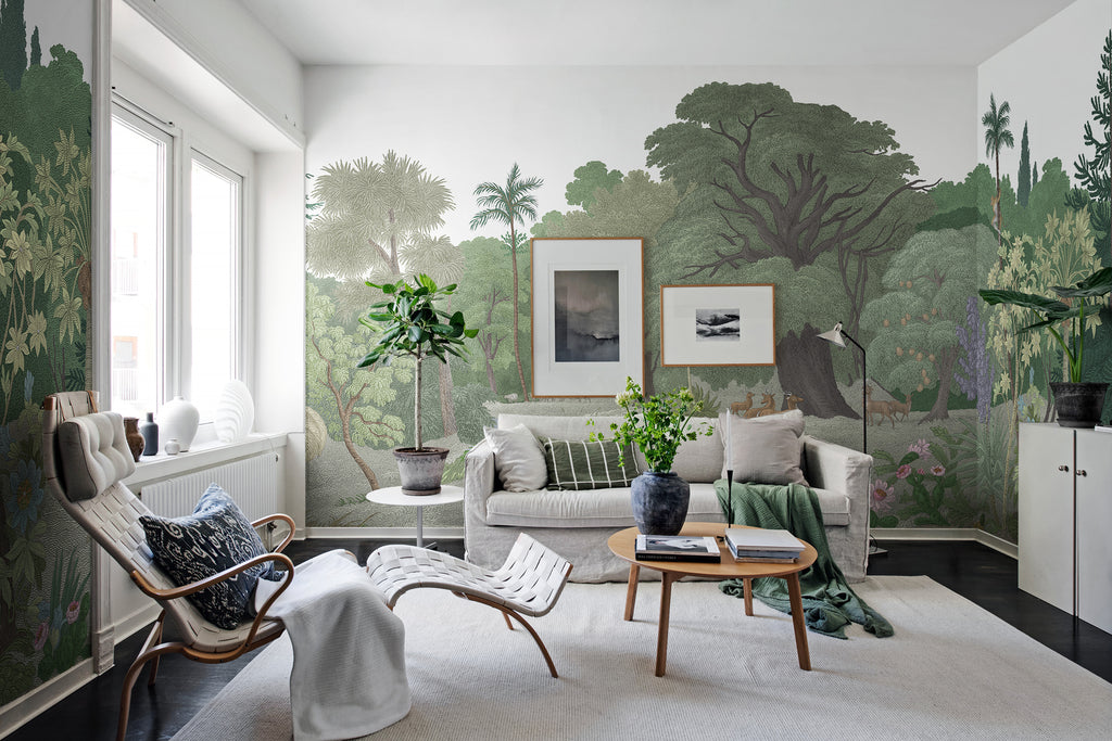 Jungle Land, Mural Wallpaper in forest green featured on a wall of a living room with white sofa, brown round table and single sofa chair adjacent to a sliding window
