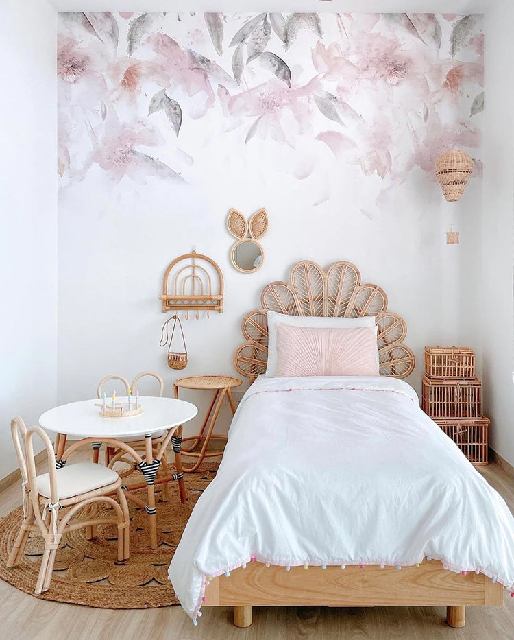 Pink Florals, Watercolour Mural Wallpaper, adorns a kids bedroom featuring a single bed with white sheets, complemented by a rattan round table and chair.