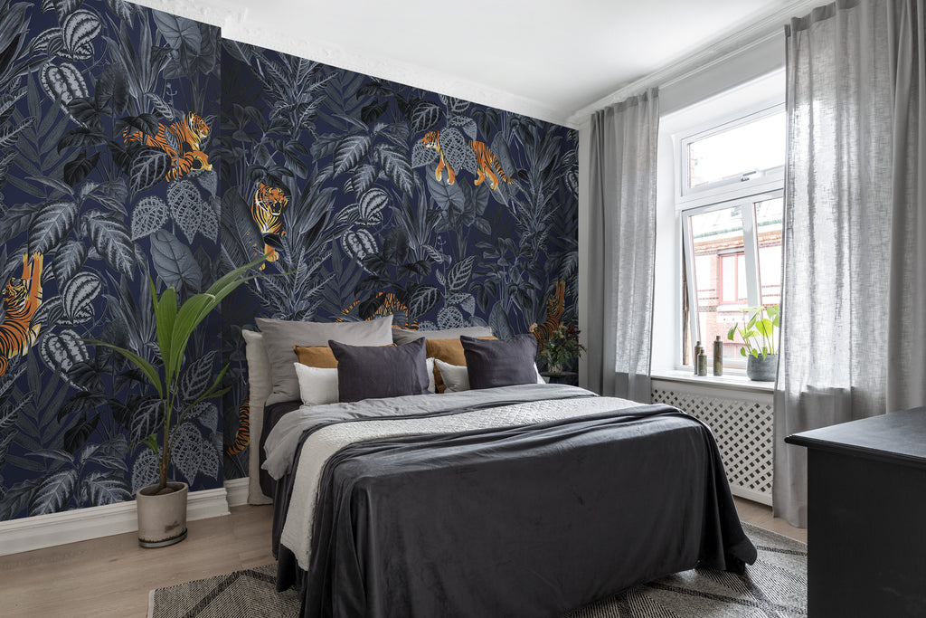 Playful Tiger, Pattern Wallpaper in dark blue colourway as seen in a cozy bedroom with light brown wood flooring, on the bed, there is black bedsheet with white throw blanket and multicolored pillows