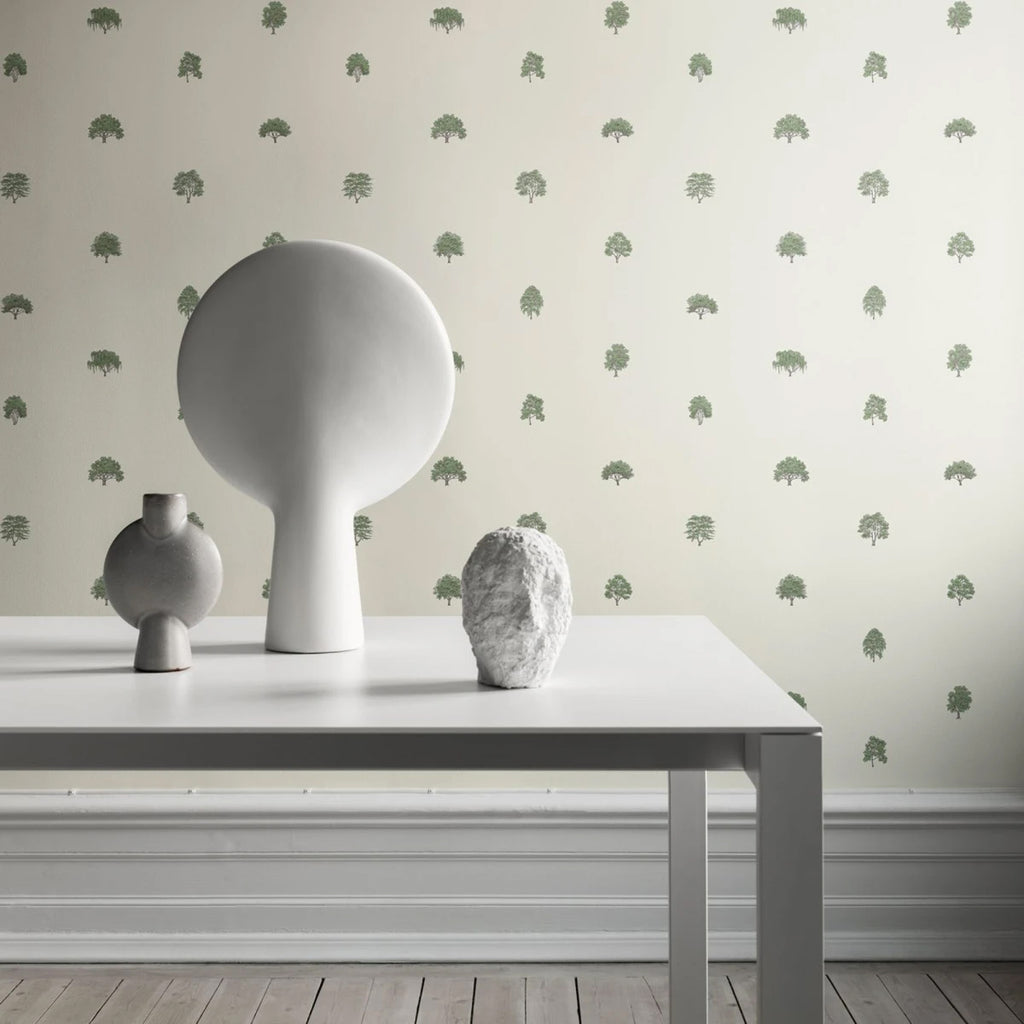 Rowena Trees Patterned Wallpaper in green featured on a wall of a room with a white table and white furniture on top
