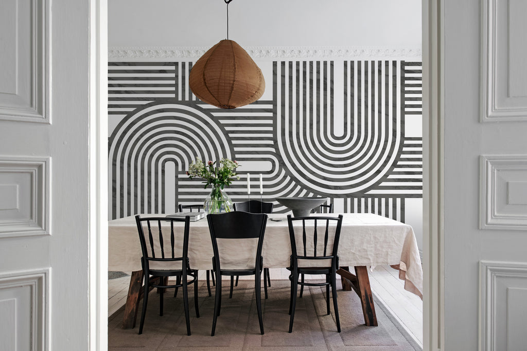 Stella Arch, Geometric Mural Wallpaper in black featured on the wall of a dining area with rectangular table and chair