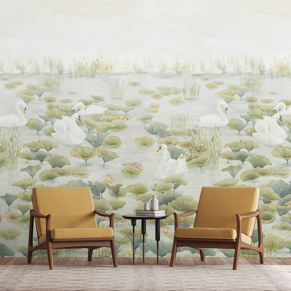 An indoor setting with Swans and Lilies, Nature Mural Wallpaper in Green featuring swans swimming amidst green lily pads and grasses. Two modern chairs with yellow upholstery and a small round table with two cups and a book create a relaxed environment.