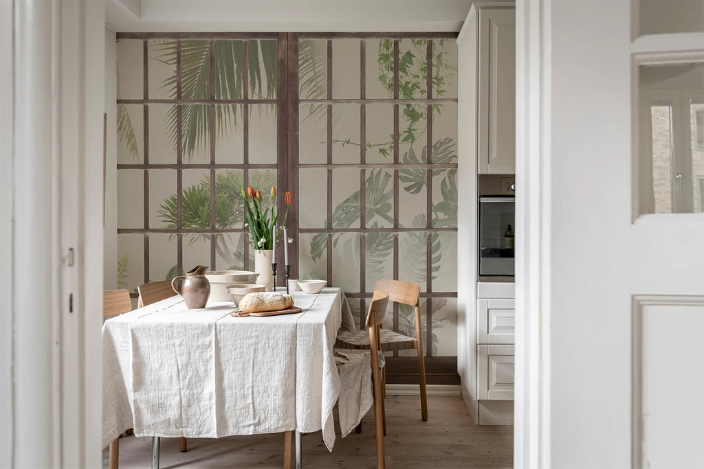 Window View, Beige Wallpaper featured on a wall of a dining area with a dining set made of wood with a white tablecloth, a wooden flooring, above the table is a copper pitcher, a bread and a vase with flowers. 