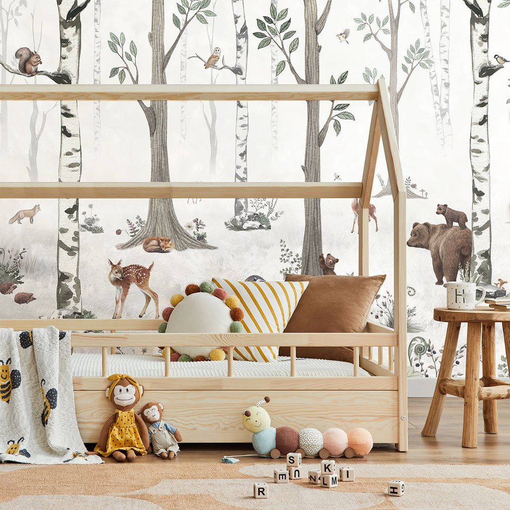 A cozy child’s bedroom with a nature-themed ‘Woodland Stroll, Animal Mural Wallpaper’ featuring bears, deers, rabbits, squirrel, owl and more. A wooden bunk bed adorned with plush toys and patterned bedding is the centerpiece. The floor is scattered with toys and blocks adding a playful touch.