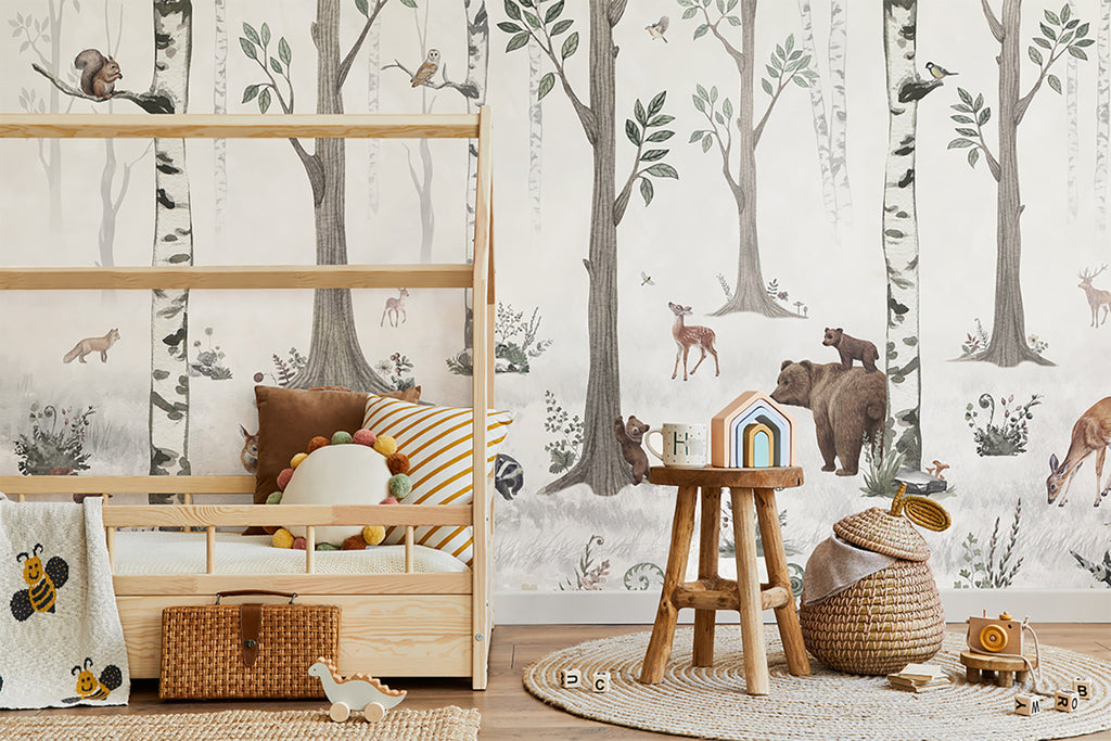 A serene children’s room featuring a wooden crib and shelves filled with toys. A woven rug and small stool add charm. The room is lit by natural light, enhancing the Woodland Stroll, Animal Mural Wallpaper featuring bears, deers, rabbits, squirrel, owl and more.