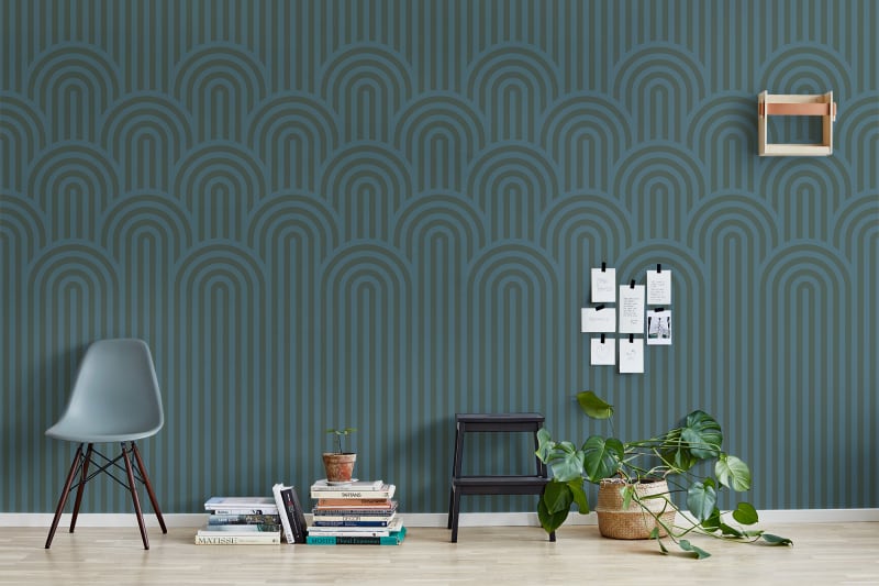 Emerald green lounge area with arch hill wallpaper. A green modern chair is present along with books and plants on the floor, placed flat against the wall