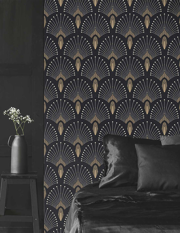 A cozy room featuring a bed with dark bedding, a sleek side table holding a tall vase with fresh flowers. The room’s ambiance is enhanced by the soft, muted lighting and the striking 1920s Fan, Geometric Wallpaper in Black.