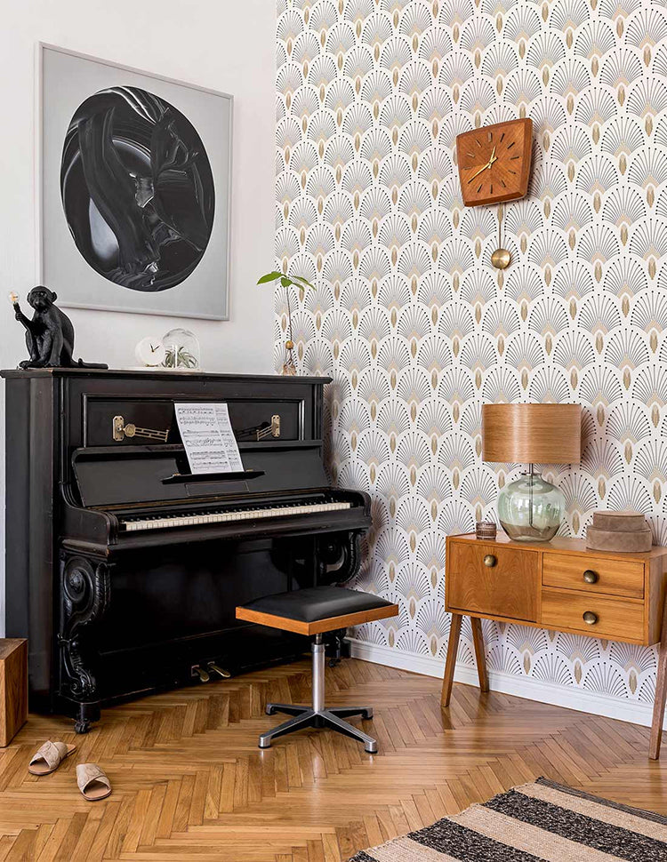A cozy room with a black piano, sheet music, a wooden cabinet, abstract art, and shoes on a polished wooden floor, all set against a 1920s Fan, Geometric Wallpaper in White.