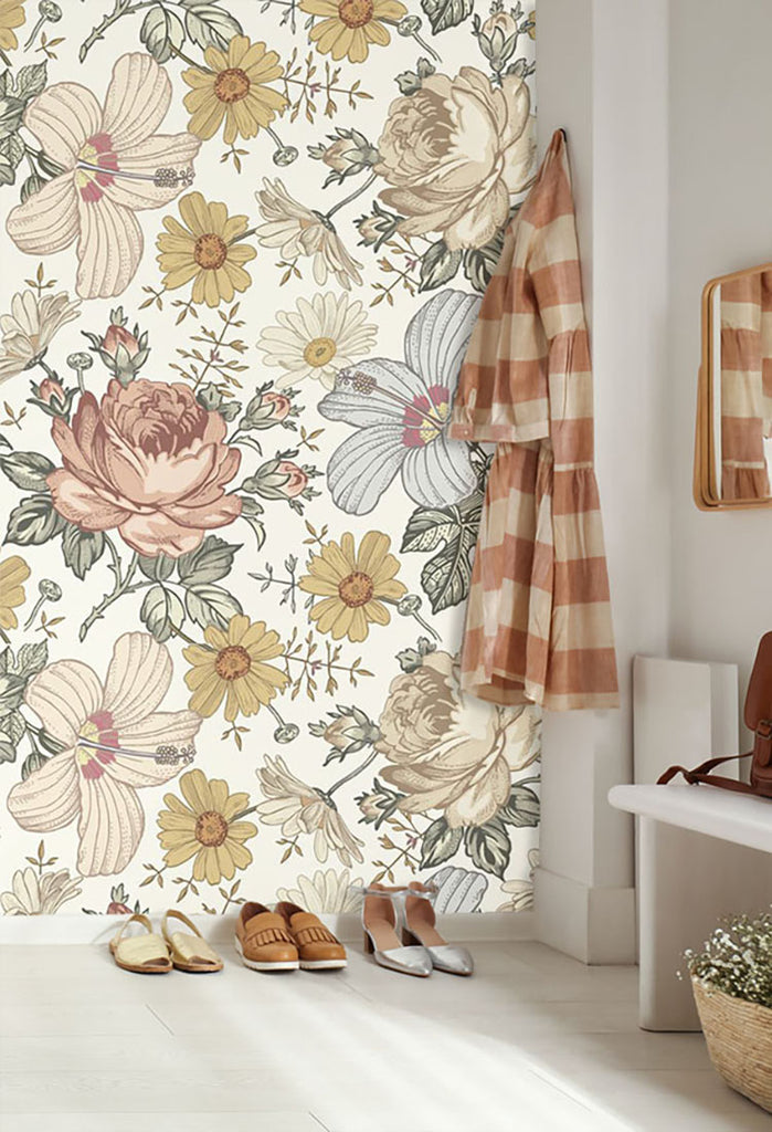 A room is transformed by the Adora, Vintage Floral Mural Wallpaper in Sand, showcasing large beige and pink flowers with gray leaves on a white background. The room is further enhanced by natural light, plaid curtains, and stylish footwear.