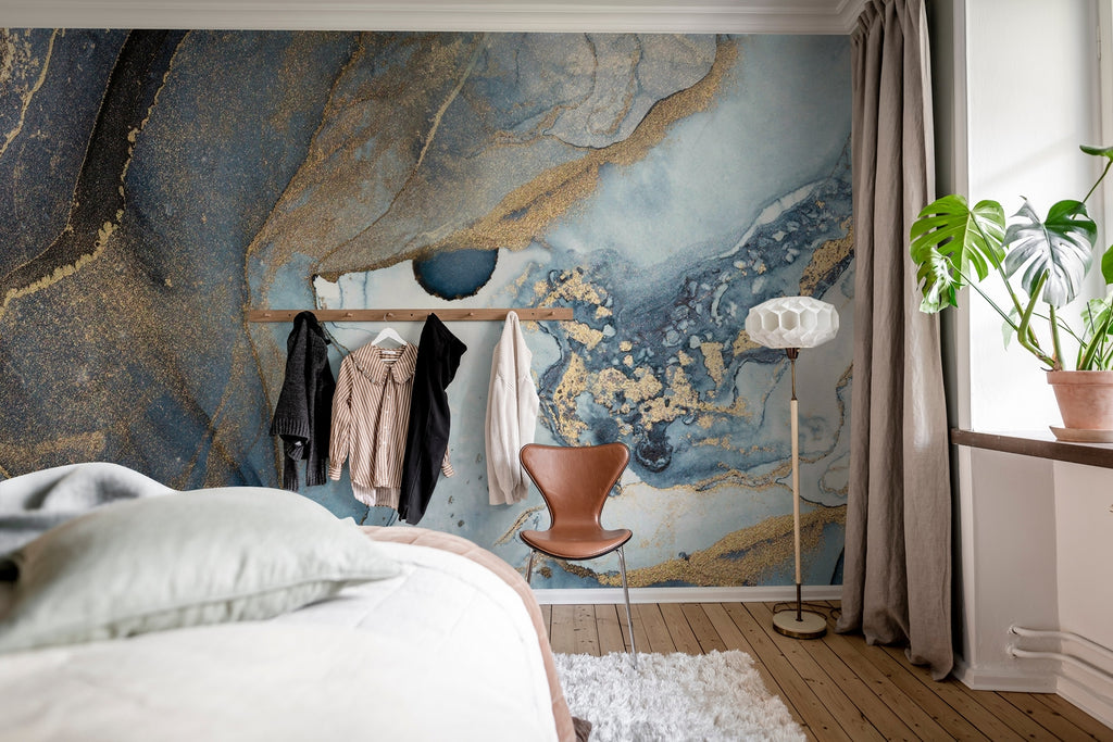 Agate Crystal Marble Texture Wallpaper in Blue featured on a wall of a bedroom with a part of the bed seen and several clothes hanging on the wall. 