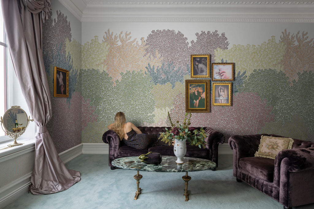 Alice Garden, Mural Wallpaper in multicolor featured in a living area with dark brown vintage sofas and glass oval table. 