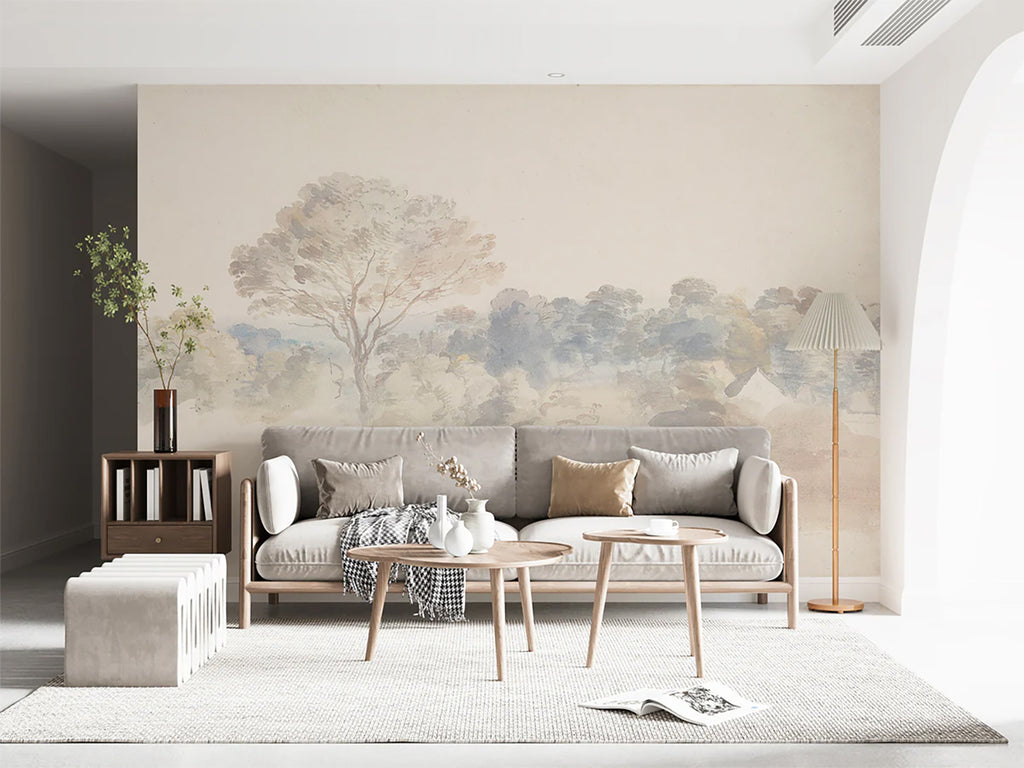 A cozy living room bathed in soft light, adorned with An Old World Arboretum watercolour mural in Vintage wallpaper. The room is furnished with a plush beige sofa laden with cushions, a rustic wooden coffee table, and a side table stacked with books. A floor lamp casts a warm glow, enhancing the room’s inviting ambiance.