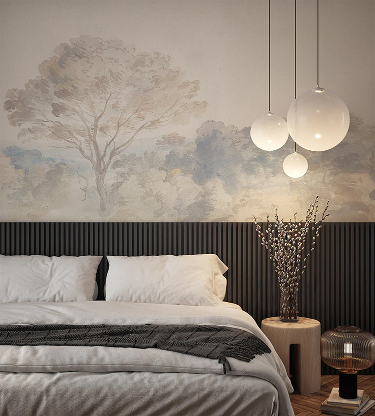 A modern bedroom with a plush bed, white bedding, and a grey throw blanket. A wooden side table holds a vase with branches. Spherical hanging lights add a contemporary touch. The room is enhanced by ‘An Old World Arboretum’ watercolour mural wallpaper in Vintage.