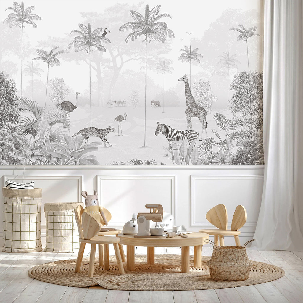 A playful Animal Paradise Mural Wallpaper in gray featuring a giraffe, flamingos, and tropical foliage adorns one wall. The room also boasts white wainscoting, light wooden flooring, and a cozy round rug. A small table with chairs and toys completes the delightful space.