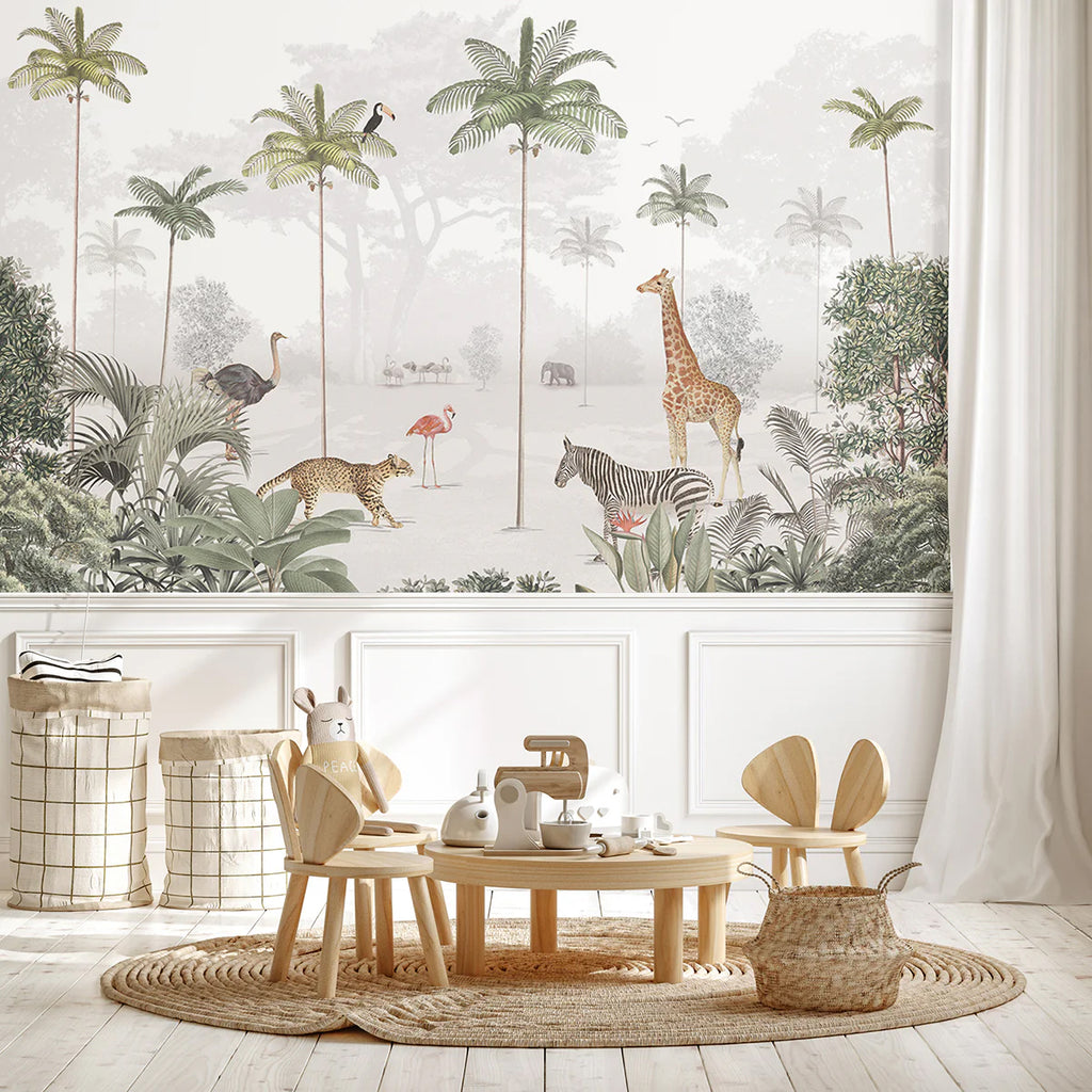 A playful Animal Paradise Mural Wallpaper in light green featuring a giraffe, flamingos, and tropical foliage adorns one wall. The room also boasts white wainscoting, light wooden flooring, and a cozy round rug. A small table with chairs and toys completes the delightful space.