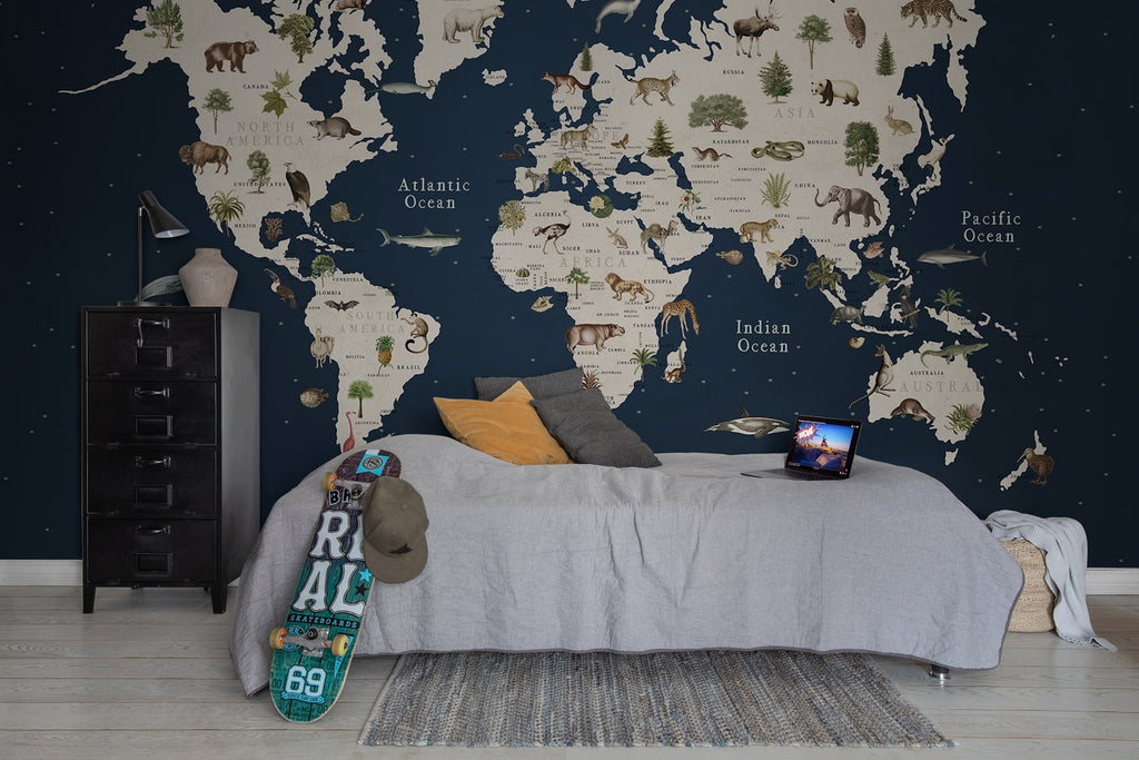 Animal World, World Map Mural Wallpaper dark blue featured on a bedroom with a bed with grey sheets, with multicolored pillows, and laptop on top, a skateboard can also be seen with a dark green cap. 