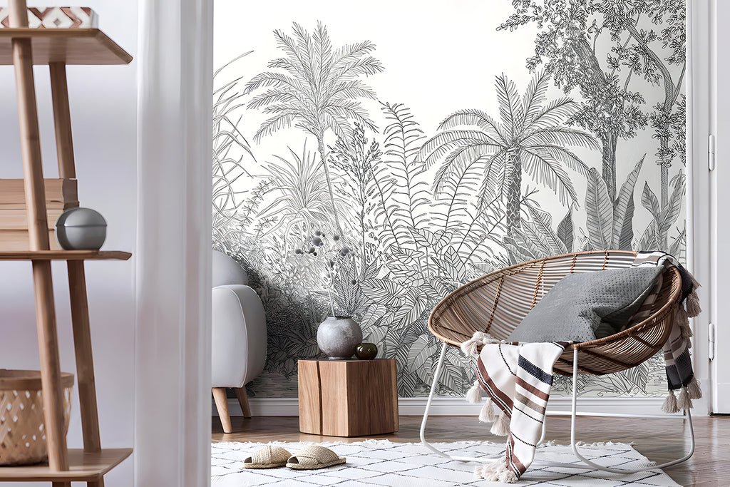 Ara's Jungle, Tropical Mural Wallpaper in dark grey, featured on a room wall. This setting is complemented by a modern rattan chair and a wooden side storage unit, which is adorned with ceramics on top.