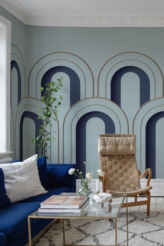 Arch Decor in Blue, Geometric Wallpaper featured on a wall of a living area with blue sofa, rattan single chair, and a glass square table