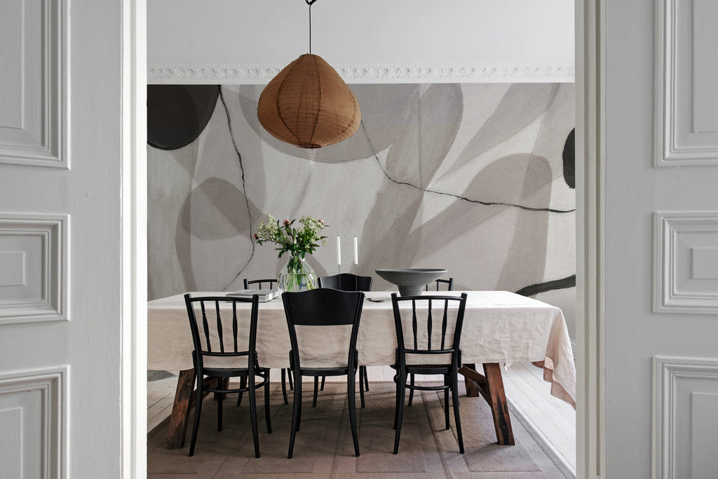 Asana, Abstract Mural Wallpaper in black white featured on the wall in a dining area with rectangular table and chairs.
