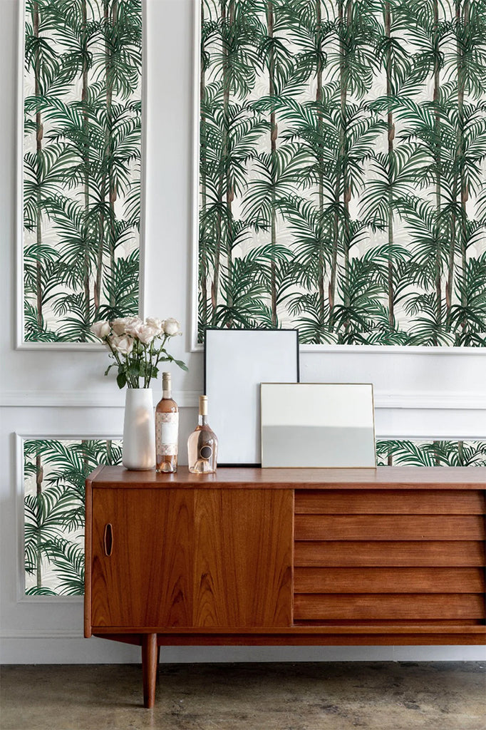 Bamboo, Tropical Pattern Wallpaper in Forest Green featured in a wall of a room with a wooden vintage sideboard with bottle, and vase on top