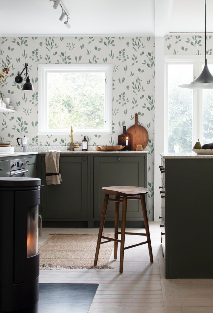Belle Foliages, Tropical Pattern Wallpaper in Green featured on a wall a kitchen area that has green shelves for countertop and a wooden barstool in the middle and a pendant light by the middle countertop