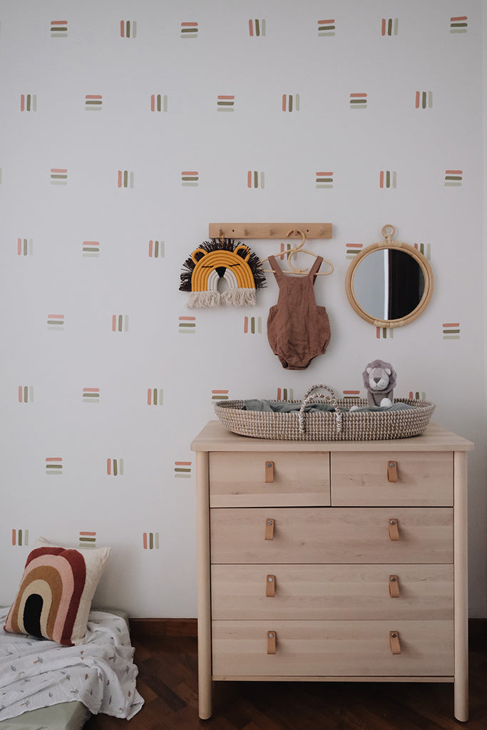 Cozy nursery room with a wooden dresser, woven basket, and baby items. Round mirror above, flanked by cute wall decorations. Bold Lines, Wall Decals in Light Green - Dark Green - Brown.