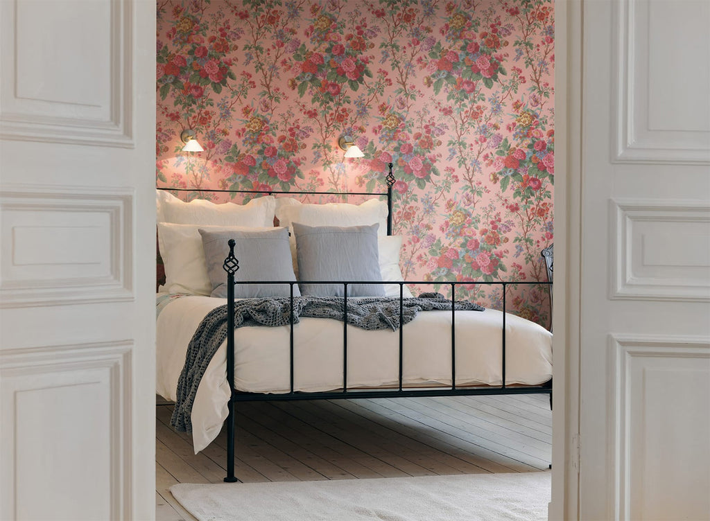 Bouquet Floral Pattern Wallpaper in Pink, featured on a wall of a bedroom with white bedsheets and grey throw blanket and pillow as seen from a door of its entrance