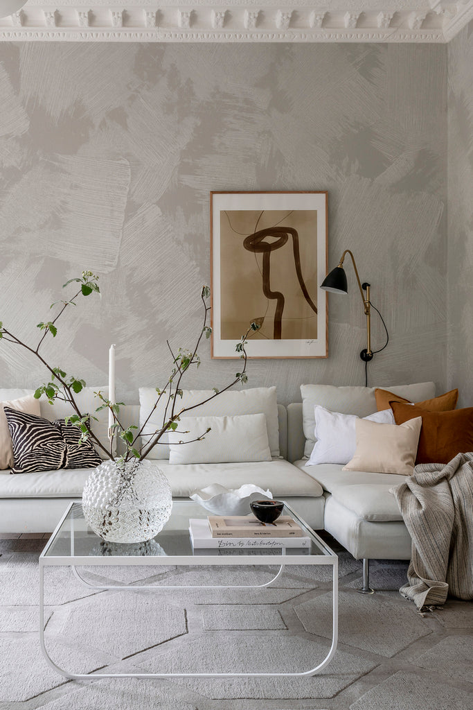 Closed up, Brush Mural Wallpaper in light grey, featured on a wall of a cozy living area with sofa and coffee table