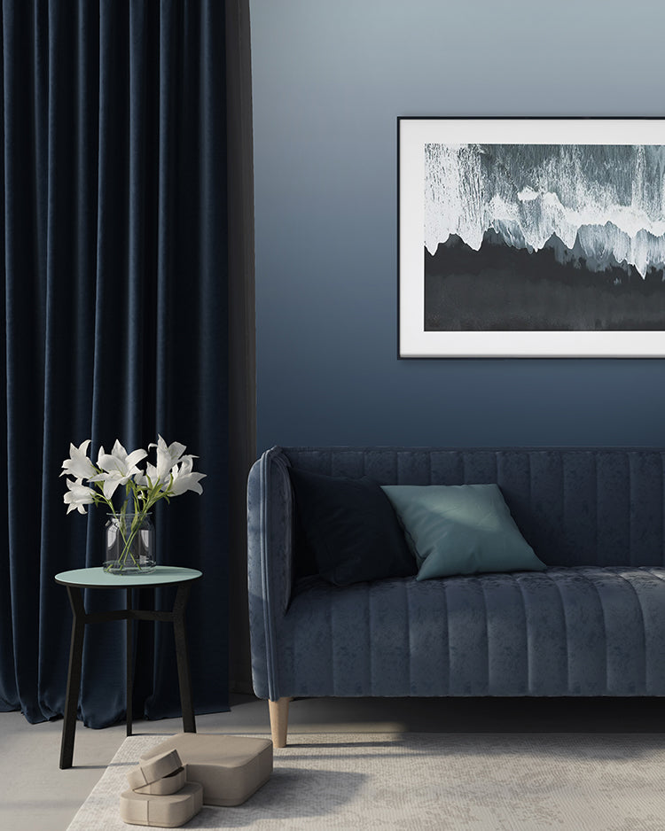 Modern room featuring Calbri Ombre Wallpaper, transitioning from deep blue at the base to a lighter hue at the top. Complemented by a dark blue velvet sofa, a green round table with white lilies, and abstract art.
