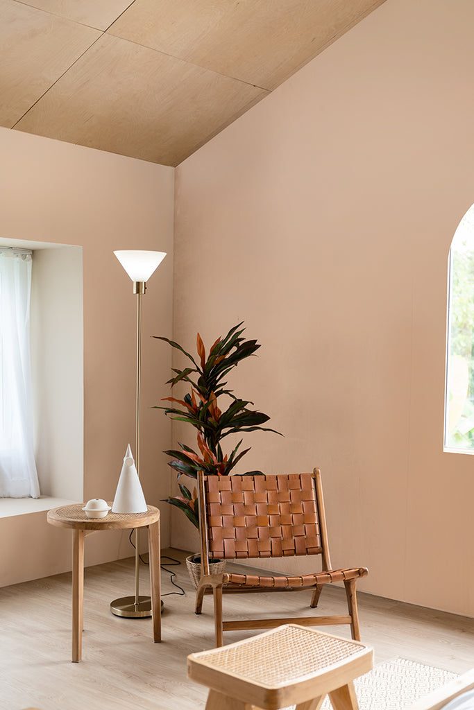 A serene room featuring a Calbri Ombre Wallpaper, a stylish leather chair, a round table with decor, an indoor plant, and a floor lamp near a window with sheer curtains.