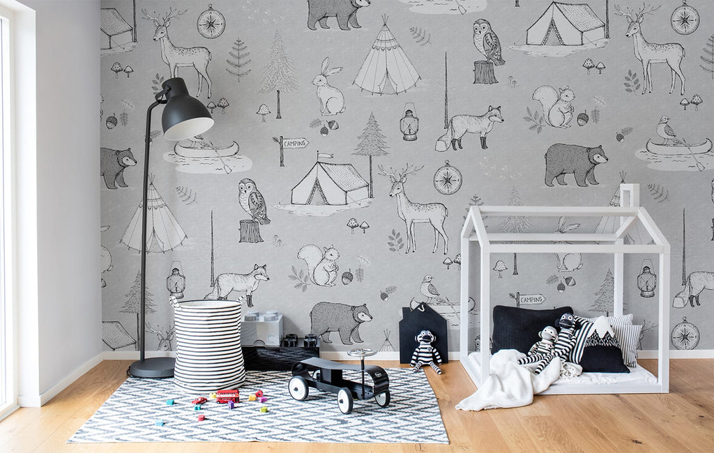 Camping Trip in Grey, Animal Pattern Wallpaper featured on a wall of kid’s playroom with a wooden playhouse and patterned floor mat on a wooden flooring with toys on the ground