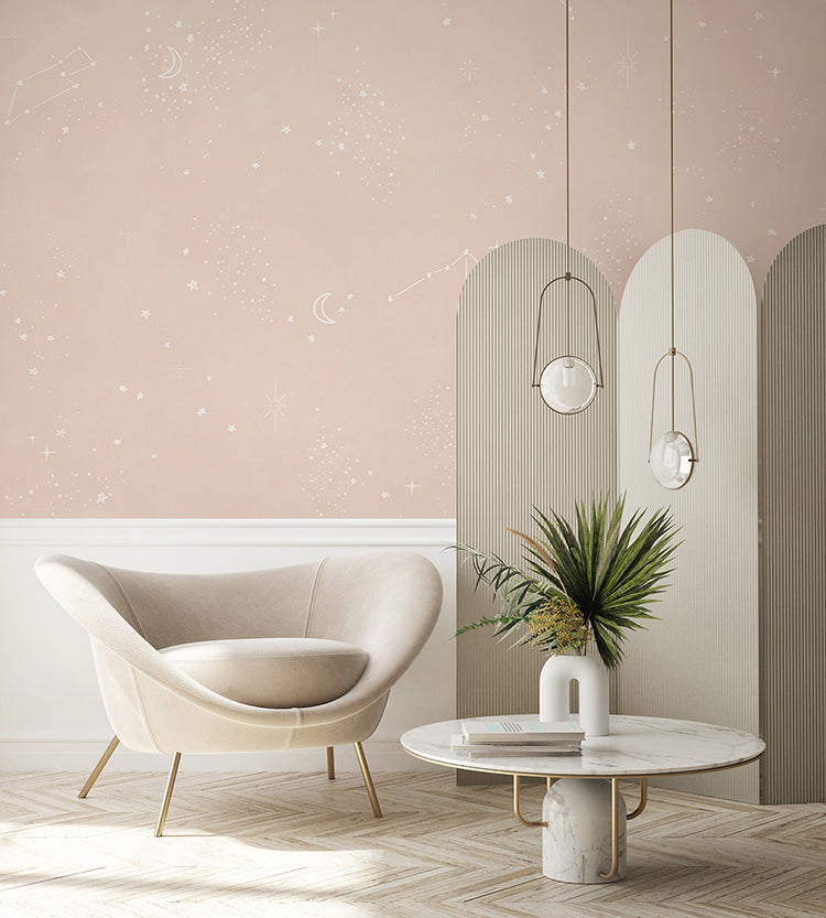 A tranquil space featuring a beige armchair with elegant gold legs, perfectly paired with a round marble table. The table holds a small plant and a decorative item, adding a touch of nature and personality to the room. Above, elegant pendant lights cast a warm glow, enhancing the cozy atmosphere. The room is wallpapered in a Chalky Stars, Pastel Pattern Wallpaper in Sand, which adds a whimsical charm to the modern elegance of the room.