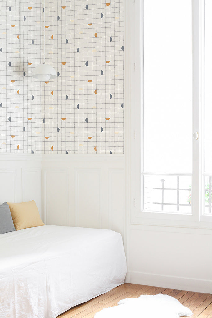 Checkerboard, Geometric Wallpaper in Clay/Grey/Beige featured in a naturally lit room with white sofa and a couple of pillows. The room has a wooden flooring and a white rag can also be seen