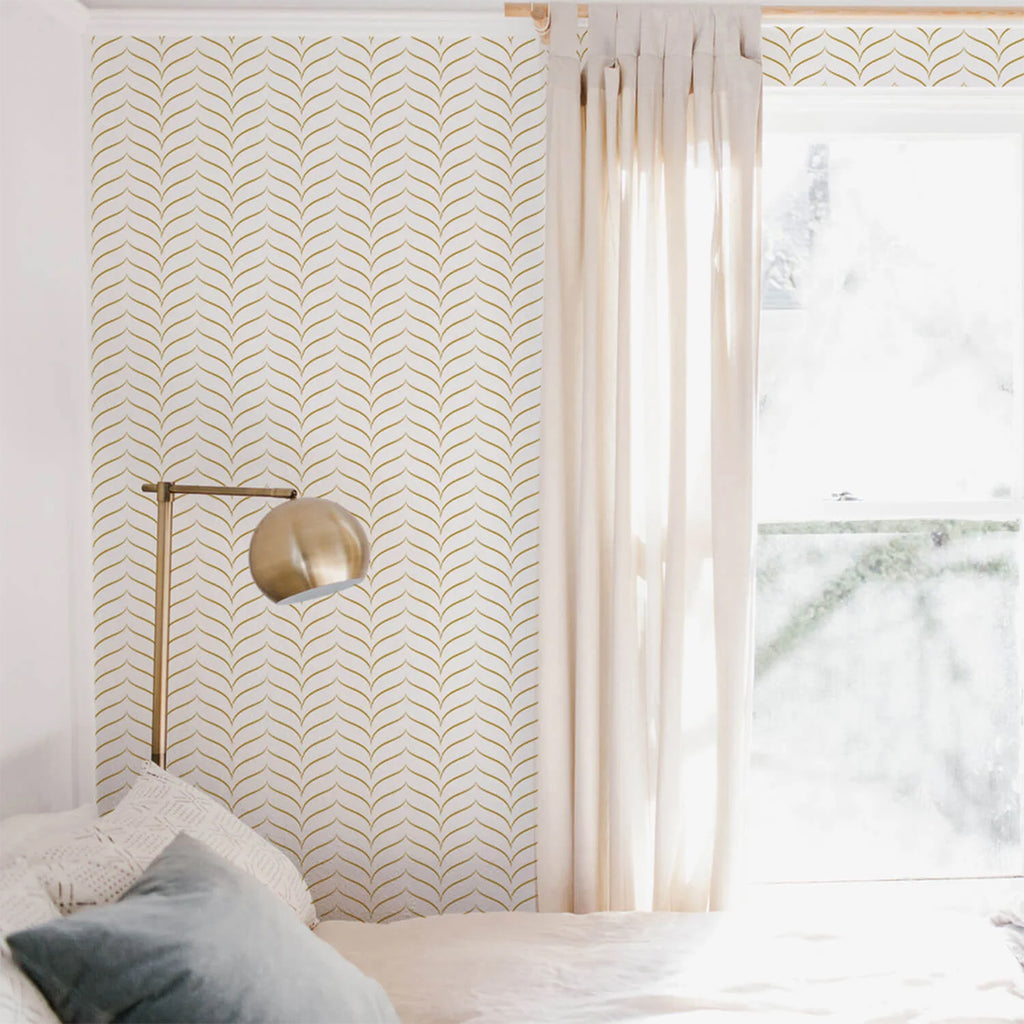 Sunlit, serene bedroom with gray bedding. Chevron, Matte Gold Pattern Wallpaper adorns a wall. A brass sconce lamp adds a modern touch. Sheer white curtains allow natural light to filter in.”