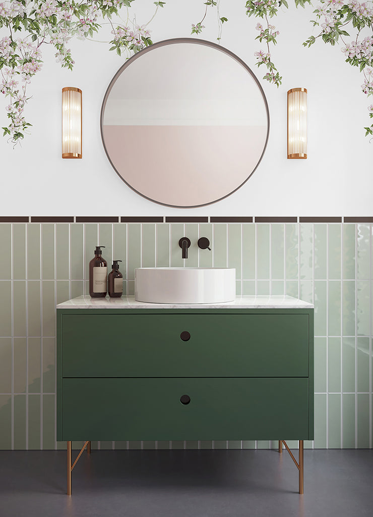 An elegant bathroom vanity area with Classic Clematis, Floral Mural Wallpaper in White featuring blooming flowers and green leaves. A large round mirror, vertical light fixtures, and a green vanity cabinet with a contemporary white basin sink complete the modern look.