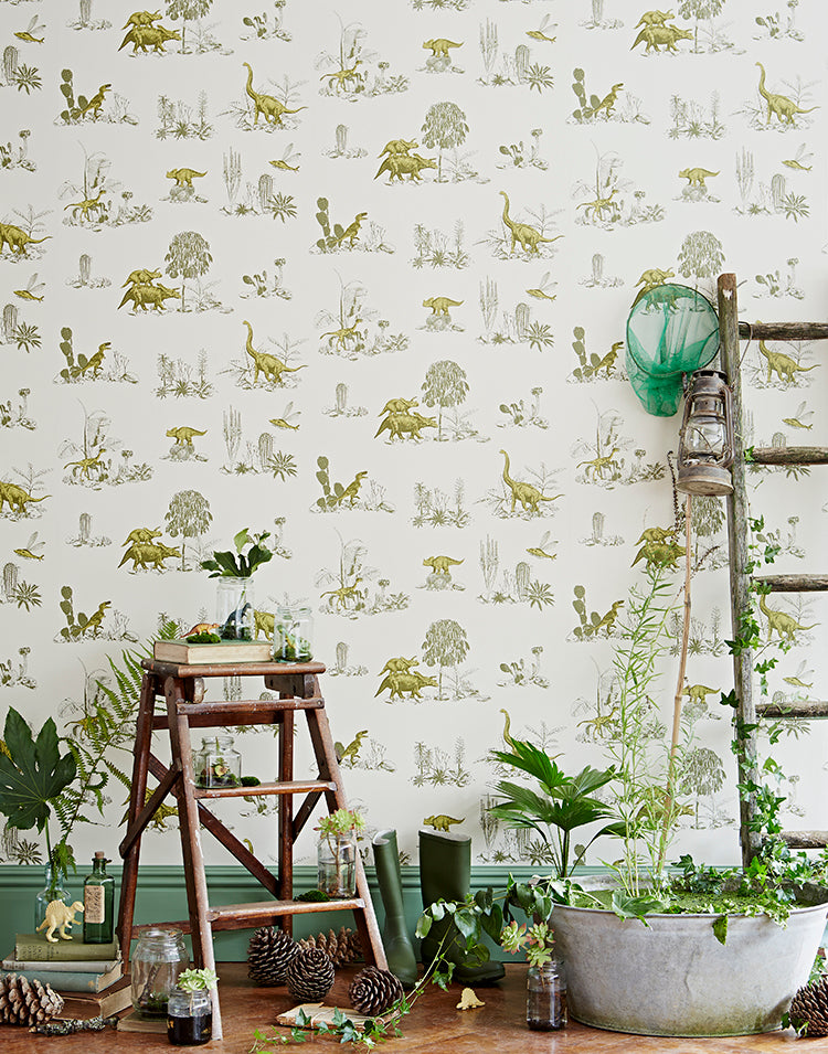 Classic Dino, Pattern Wallpaper in Green featured on a wall of a room with an Indoor setting with a rustic ladder and wooden stool. Various potted plants, jars, and a green netted catch-all add to the decor.