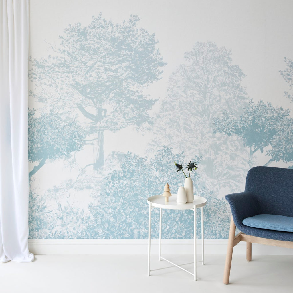 Classic Mua, Mural Wallpaper in Blue transforms a serene room, with a white round table with a vase and decorative items, a stylish blue chair, and a glimpse of a white curtain.