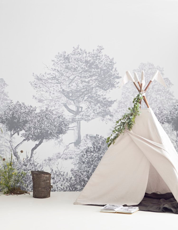 Classic Mua, Mural Wallpaper in Grey sets a cozy and elegant living room with a detailed forest scene, a white teepee adorned with green vines, a rustic bucket with greenery, and an open book on the floor.