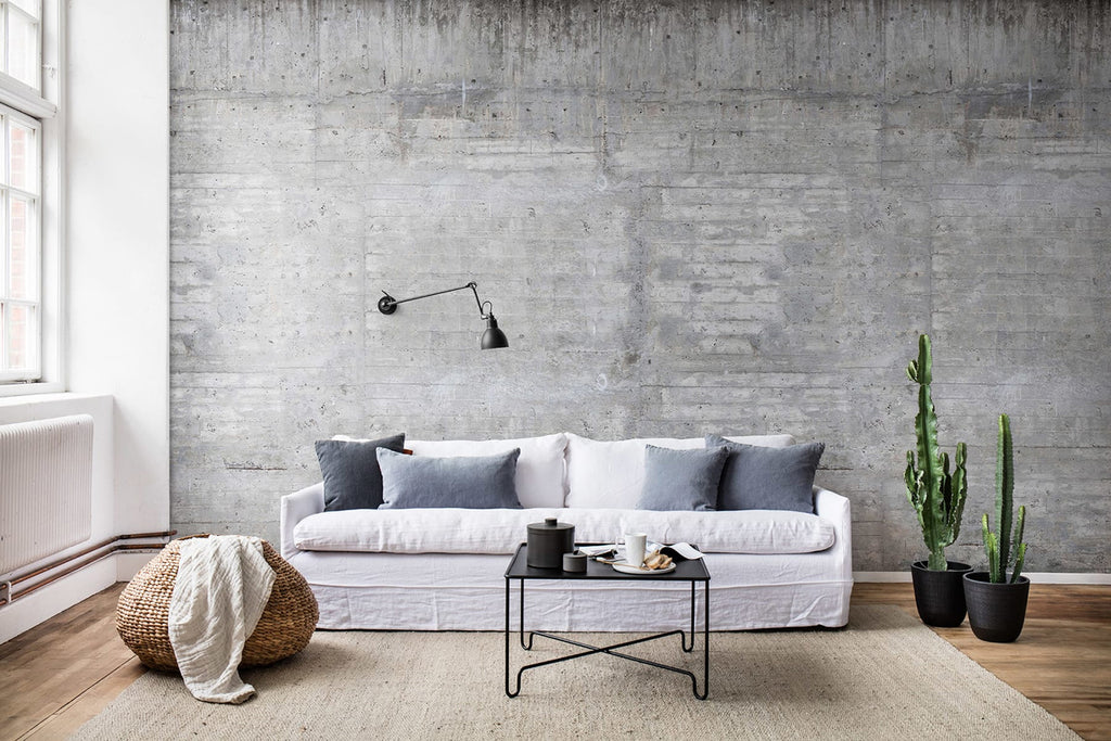 A modern minimalist living room with a Concrete Grey, Wallpaper. Features include a white sofa with grey cushions, a black coffee table, and green plants adding a touch of nature.